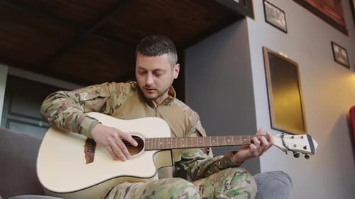 Man in Camouflage Plays Acoustic Guitar on Sofa