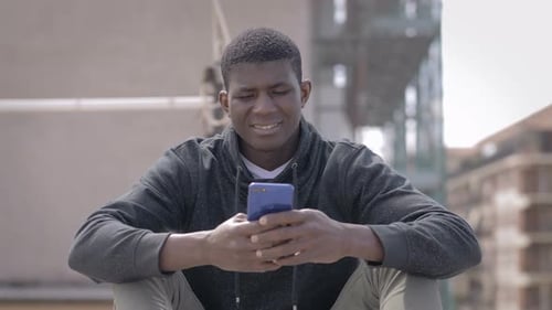Young Man Using Smartphone Sitting Outdoors