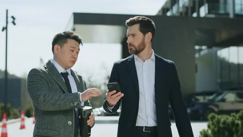 Two Attractive Business Men Walking Talking Discussing on Street in Modern City Near Business Center