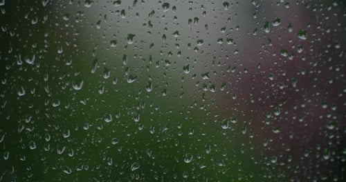 Window in focus while raindrops fall on it in the out-of-focus exterior.