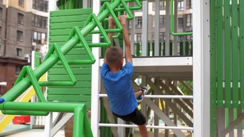 An Active Boy Climbs on a Playground with a Metal Ladder and Horizontal Bars