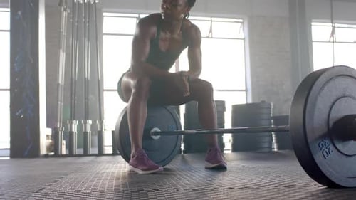 Resting on barbell, woman in gym taking break from weightlifting workout