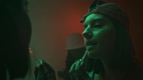 Young Lady with Short Hair and Cap Applying Lip Gloss in Nightclub Washroom