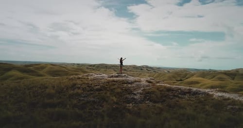 Young Woman Standing with Open Arms on Top of a Hill Enjoying the Landscape