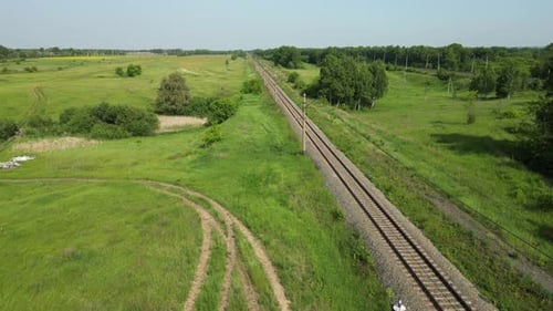 Sonnenbeschienene Eisenbahnstrecke, die durch eine üppige grüne Wiese führt und die weitläufige ländliche Landschaft enthüllt