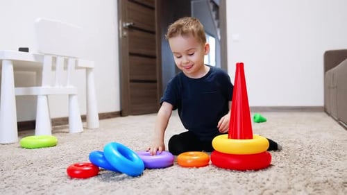 Das
lächelnde kaukasische Baby baut eine Spielzeugpyramide zusammen. Fröhliches Kind legt die Ringe auf die Basis.