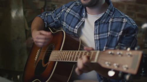 Man plays guitar while rehearsing a song in a home studio in a garage.