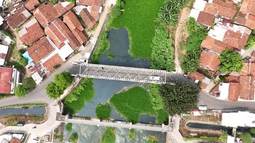 Drone footage from top of small bridge with town house and green river
