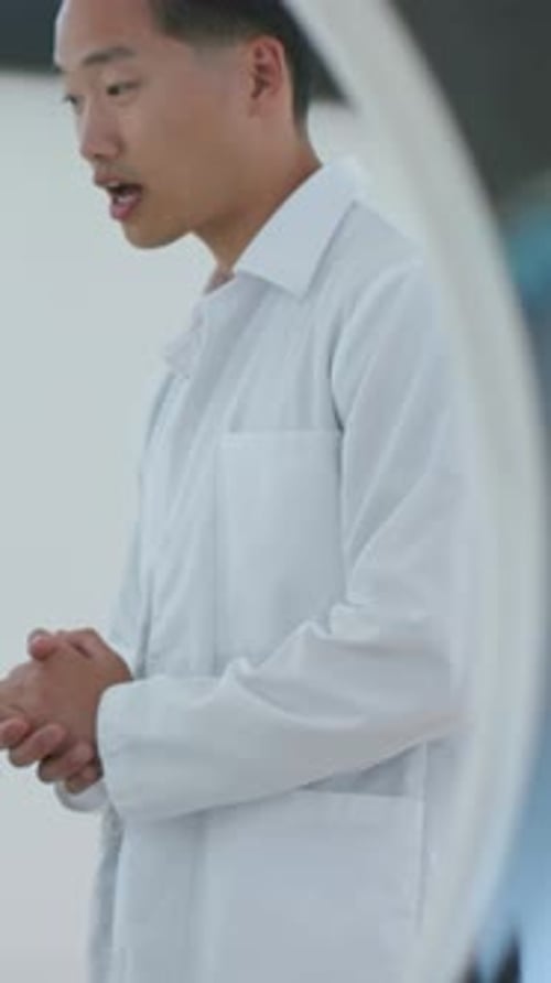 Vertical video: Responding to prompt, Korean man in white lab coat gesturing in clinic, curved unit