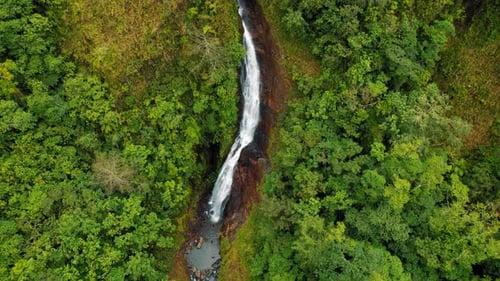 Aerial view of a long waterfall cutting through dense forest in Costa Rica