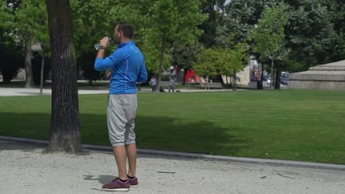 Young Male Jogger Resting and Drinking Water in City Park, Super Slow