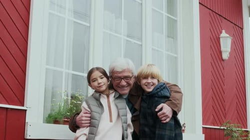 Grandfather and Grandchildren Embracing Outside Red Suburban House