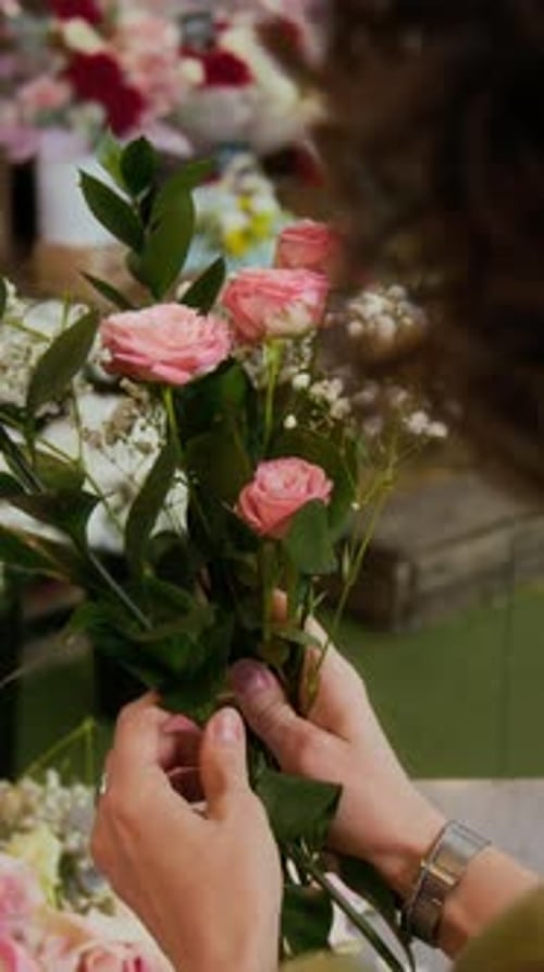 Fleuriste aux cheveux bouclés créant un bouquet à l'aide de roses roses et de gypsophilas blancs