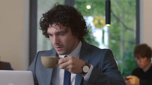 Focused Businessman Drinking Coffee and Using Laptop in Cafe