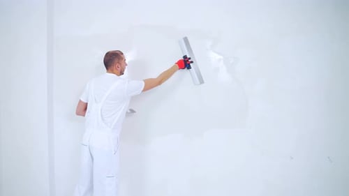 Man Smoothing Plaster on White Wall Indoors