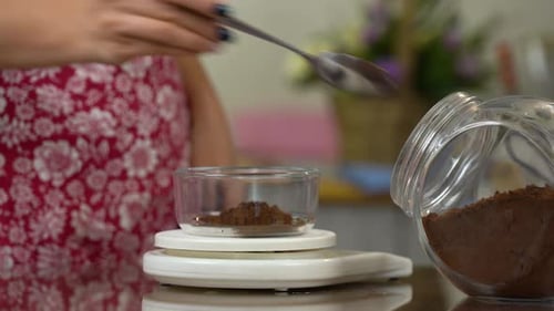 Woman Weighing Cocoa Powder with Spoon in Kitchen