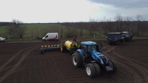 Blue tractor with yellow seeder working on the field in Ukraine OA