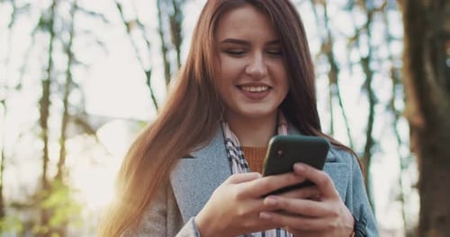Close Up of Young Beautiful Caucasian Woman Walking in Park Smiling and Using Smartphone Outside