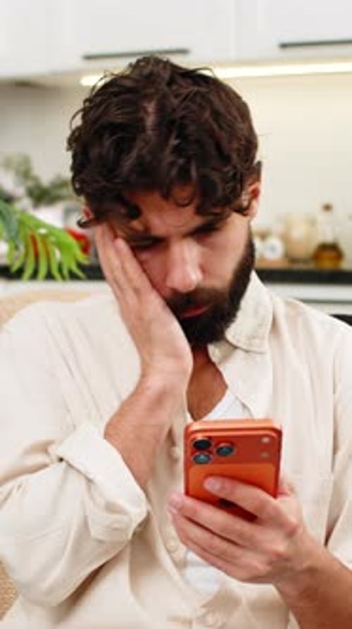 Man Using Phone in Home, Touching Hair in Thought