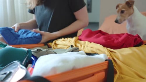 Woman packing colorful clothes into orange suitcase