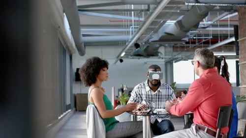 African american businessman wearing vr headset while colleagues watching him at office