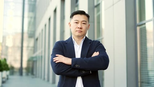 Portrait of a confident asian businessman in formal suit standing on the street near office building