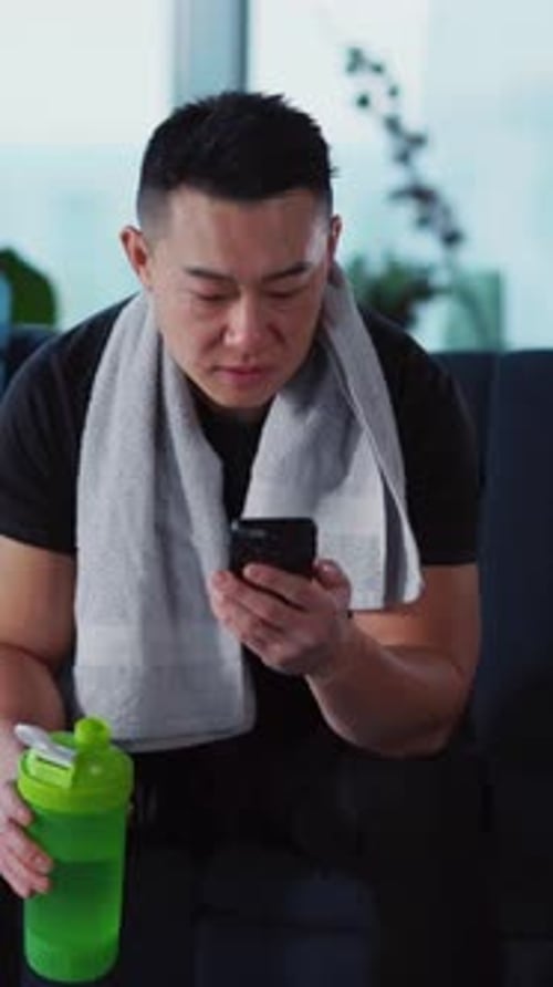 A Man is Checking His Phone After Completing an Intense Workout Session at the Gym