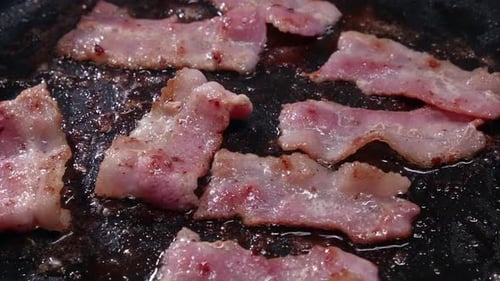 Fatty bacon strips shrink as they cook, sizzle in hot frying pan