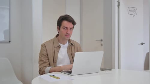 Young Creative Man with Pointing Gesture at Camera While Working on Laptop