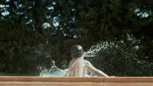 Boy in goggles leaps into pool as water splashes in air, view from side