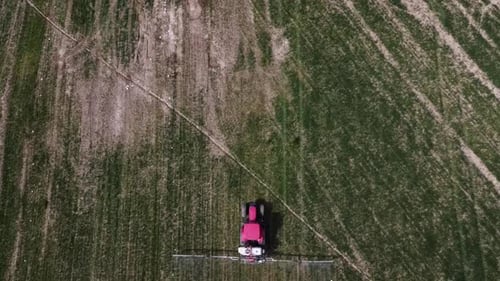 Aerial view of farming tractor spraying on field with sprayer, herbicides and pesticides insecticide