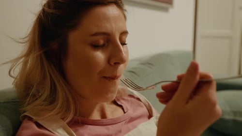 Close up pregnant enjoying the cake with eyes closed sitting on couch.