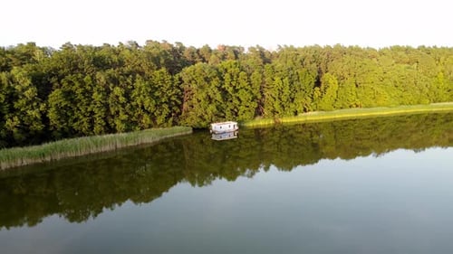 Casa flotante flotando en un lago junto a un junco durante la puesta de sol en Brandeburgo, Alemania