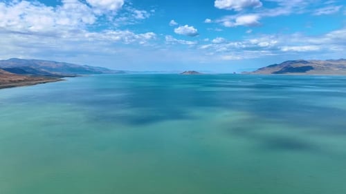 Blue sky with white clouds reflect in the vast waterscape of a lake.