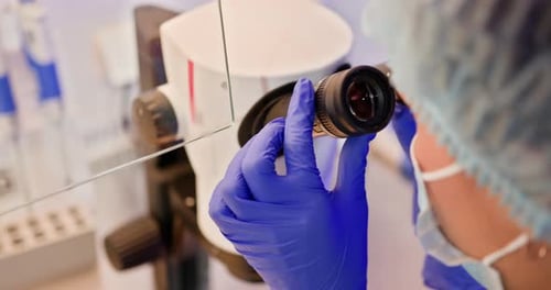 Gloved Lab Worker Adjusting Microscope in Laboratory
