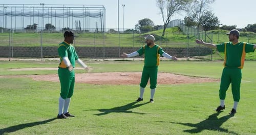 Performing warmup baseball teammates rotating arms on outfield grass with batting cage netting