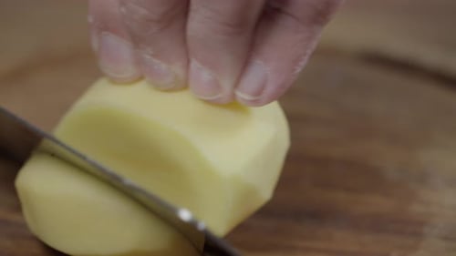 Close-up of chef cutting raw potatoes into slices. No face.