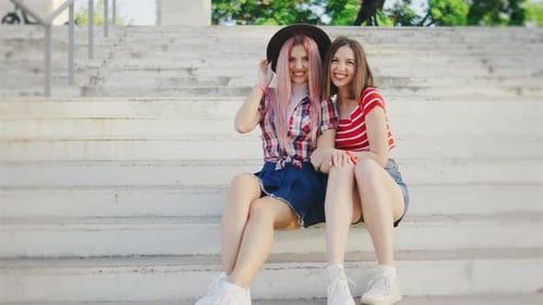 Portrait of Two Beautiful Girls are Sitting on the Steps in the Park and Talking to Each Other