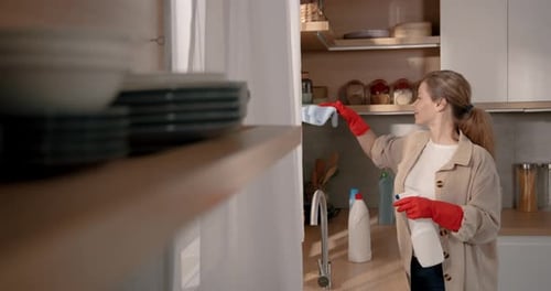 Woman Cleaning Kitchen Shelves with Gloves and Sprays