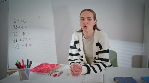 Woman Explains Lesson at Desk with Whiteboard