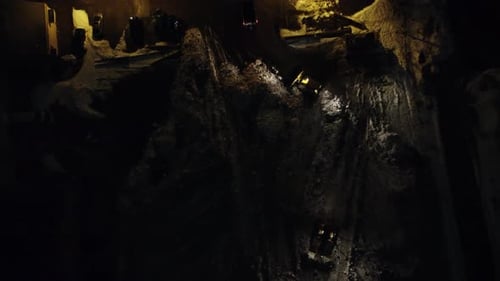 Aerial Birds Eye View At Night Showing Trucks And Snowplow Dumping And Moving Snow At Storage Site.