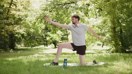 Sporty Fit Young Man Doing Workout Yoga Warrior Pose in Park on a Sports Mat Arms Outstretched