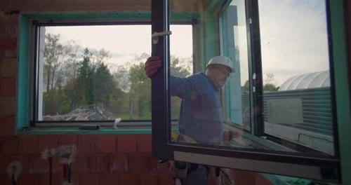 Worker adjusting window frame on construction site, checking for accurate installation in