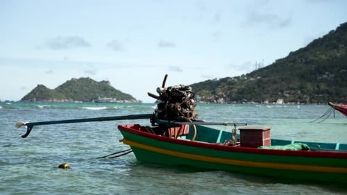 A vibrant, colorful boat with a visible engine is anchored in the clear, turquoise waters near a lus