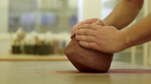 Pottery craftsman hands rolling raw clay material preparing creation on workshop surface