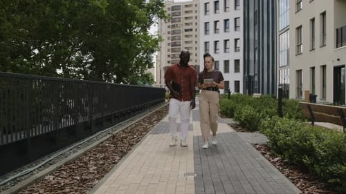 Coworkers Walking in Urban Park and Discussing Business Issues