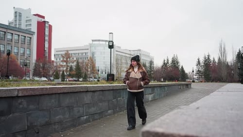 Young Girl Walking Slowly on Urban Autumn Pathway with Trees and City Buildings