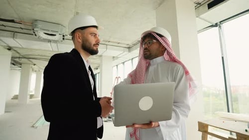 Engineers Discussing Building Plans on Laptop in Unfinished Building