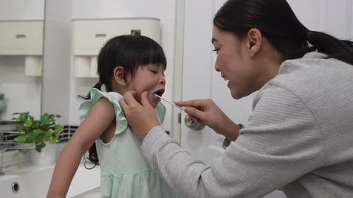 Woman Helping a Child Brush Her Teeth in Bathroom