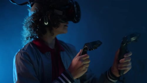 Closeup In a Dimly Lit Room at a VR Club a Teenager Wearing a VR Helmet and Holding Controllers